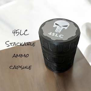 May include: Black stackable ammo capsule with a gray top featuring a white skull graphic and the text "45LC". The words "Stackable", "Ammo", and "Capsule" are written in black on the left side.