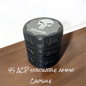 Könnte beinhalten: Schwarze, stapelbare Munitionskapsel mit grauem Deckel, Totenkopf-Logo und dem Text "45acp". Die Kapsel hat ein strukturiertes Design und die Worte "45 ACP STACKABLE AMMO CAPSULE" sind auf der Oberfläche geschrieben.