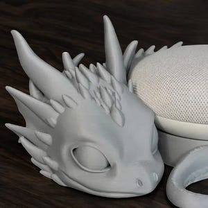 May include: A gray 3D printed dragon head with a spiky design. The dragon has a closed eye and a textured surface.