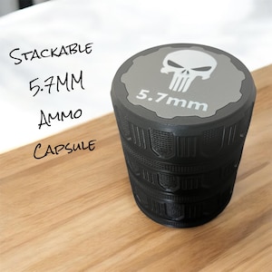 May include: A black stackable capsule with a textured grip. The top is grey with a white skull graphic and the text "5.7mm". The side of the capsule has the text "Stackable 5.7MM Ammo Capsule".