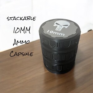 May include: A black stackable 10mm ammo capsule. The top has a gray surface with a white skull graphic and the text "10mm". The text "Stackable", "10MM", "Ammo", and "Capsule" is written in black on the left side.