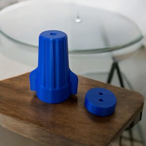 May include: A blue plastic wire connector with a ribbed design and two holes. The connector is designed to connect electrical wires together.