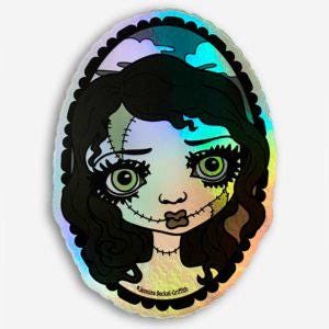 May include: Holographic sticker featuring a stylized illustration of a doll's face with stitched features. The doll has large green eyes, black hair, and a sad expression. The sticker has a scalloped edge and a rainbow sheen.