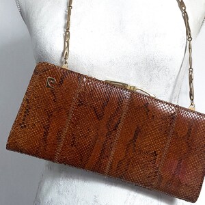 May include: A brown snakeskin clutch bag with a gold chain strap. The bag has a gold clasp and a small gold letter 'P' on the front.