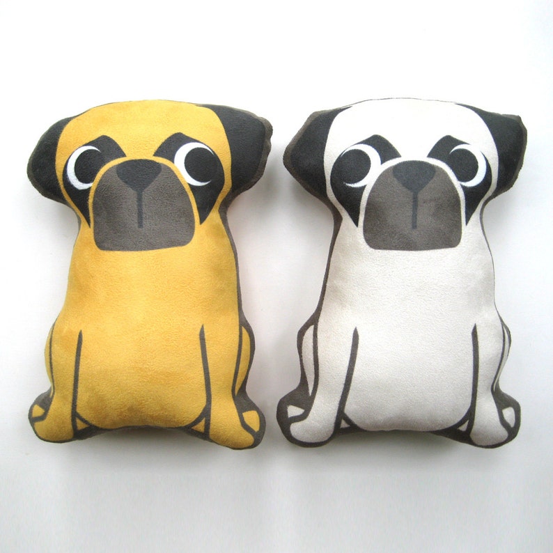 Puede incluir: Dos juguetes de peluche de perro pug, uno amarillo y otro blanco, con ojos y nariz negros. Los pugs est&aacute;n sentados con las patas extendidas.