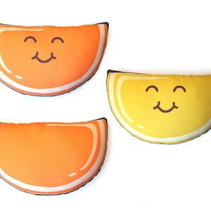 Puede incluir: Tres cojines de felpa con forma de rodajas de fruta. Dos rodajas de naranja y una rodaja de lim&oacute;n amarillo, cada una con una cara sonriente. Los cojines tienen un borde blanco y un contorno marr&oacute;n. Los cojines est&aacute;n sobre un fondo blanco.
