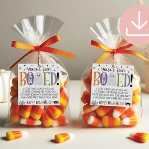 May include: Two clear plastic bags filled with orange, yellow, and white candy corn, tied with orange ribbons. Each bag features a white tag with the text You've been BOOED! A little ghost came by your way, to sprinkle fun on this spooky day.