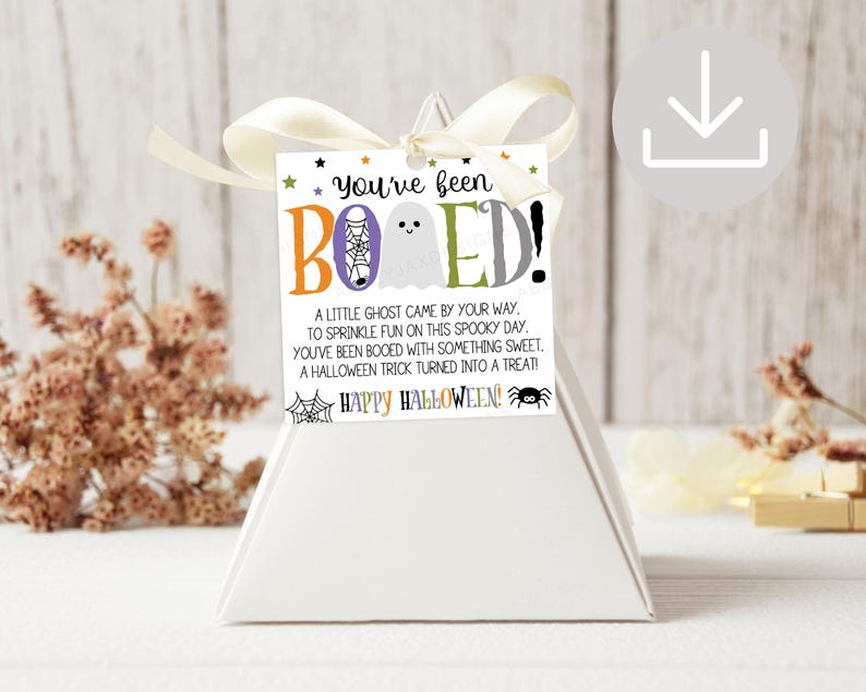 May include: A square white gift tag with a cream ribbon, featuring the text You've been BOOED! with a ghost, spider web, and spider graphic. The tag includes a poem about Halloween treats and the phrase Happy Halloween in colorful lettering.