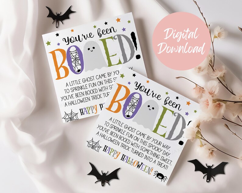 May include: Two square white cards featuring the text You've been BOOED! with a ghost, spiderweb, and colorful lettering. The cards include the poem A little ghost came by your way, to sprinkle fun on this spooky day. You've been booed with something sweet, a Halloween trick turned into a treat! Happy Halloween.
