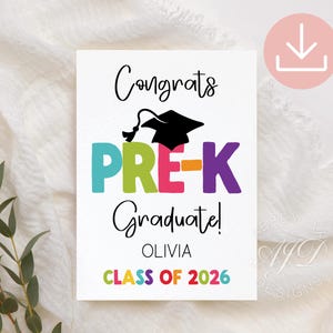 May include: A white graduation announcement with the words "Congrats Pre-K Graduate!" in black script. The word "PRE-K" is in colorful block letters, and a black graduation cap sits above it. The announcement includes the name "Olivia" and "Class of 2026".