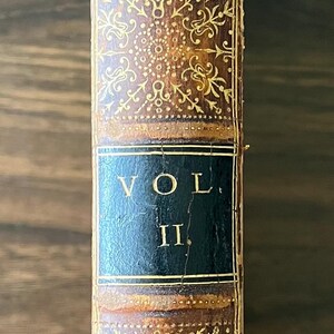 May include: A vintage leather-bound book titled "Emerson's Essays, Vol. II" with gold-leaf embellishments and a red spine.