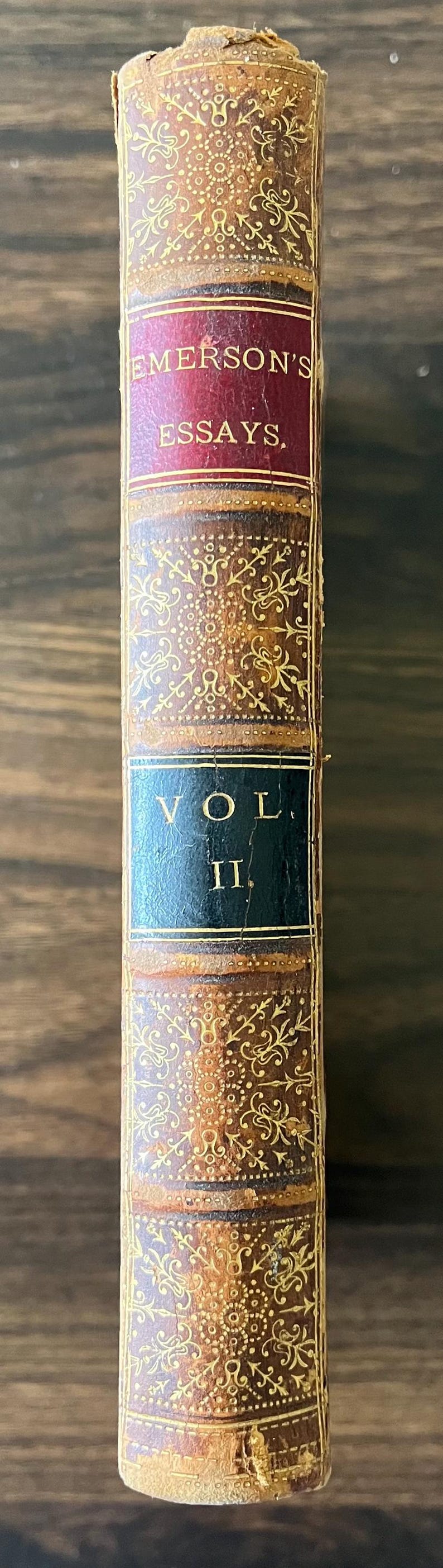 May include: A vintage leather-bound book titled "Emerson's Essays, Vol. II" with gold-leaf embellishments and a red spine.