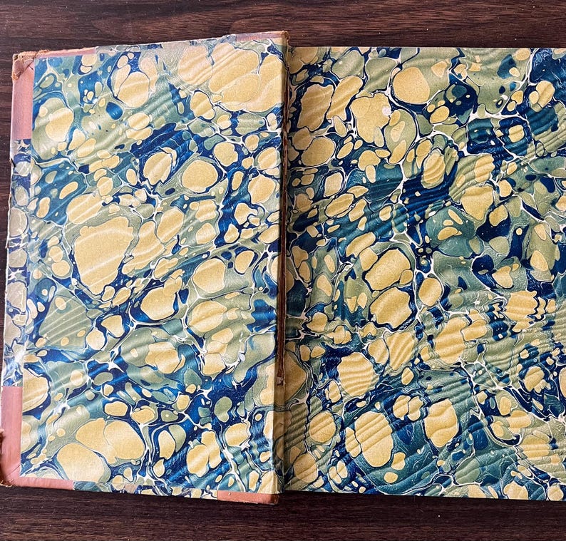 May include: Close-up of the marbled paper cover of a book. The cover is a mix of blue, green, and yellow swirls.