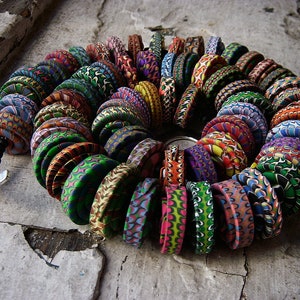 Può includere: Una collana colorata fatta di perline rotonde in argilla con motivi. Le perline sono disposte a spirale e infilate su una catena d'argento.