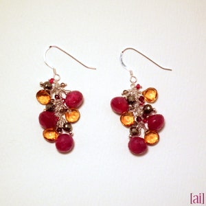 May include: A pair of dangle earrings with a cluster of red, orange, and brown gemstones. The earrings are made of silver and have a delicate, feminine design.