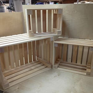 May include: Three rectangular wooden crates constructed from light-colored unfinished slats. The crates feature vertical side panels and horizontal base slats with reinforced corner blocks. The set includes one large crate and two smaller crates of identical size.