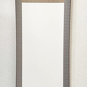 Könnte beinhalten: Eine traditionelle japanische Schriftrolle mit einem leeren weißen Bereich für Kunstwerke oder Kalligraphie. Die Schriftrolle hat einen beigen oberen und unteren Bereich, einen grau gemusterten Mittelteil und dunkelbraune Akzente.