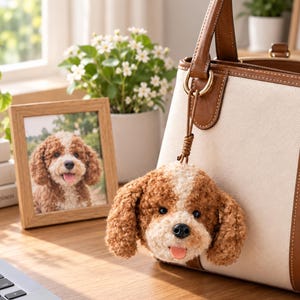 May include: A plush dog head keyring with curly brown and white fur, black eyes, a black nose, and a pink tongue, attached to a cream and brown leather handbag. The keyring features a soft, textured appearance and a small brown cord loop.