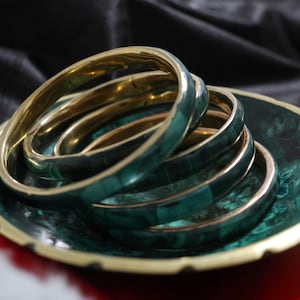 May include: A set of green and gold bangles and a matching dish. The bangles have a malachite-like appearance with gold rims. The dish features a similar green pattern and gold trim, forming a coordinated jewellery set.