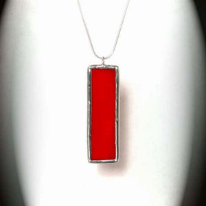 May include: A silver chain necklace with a red rectangular pendant. The pendant is made of stained glass and has a silver frame.