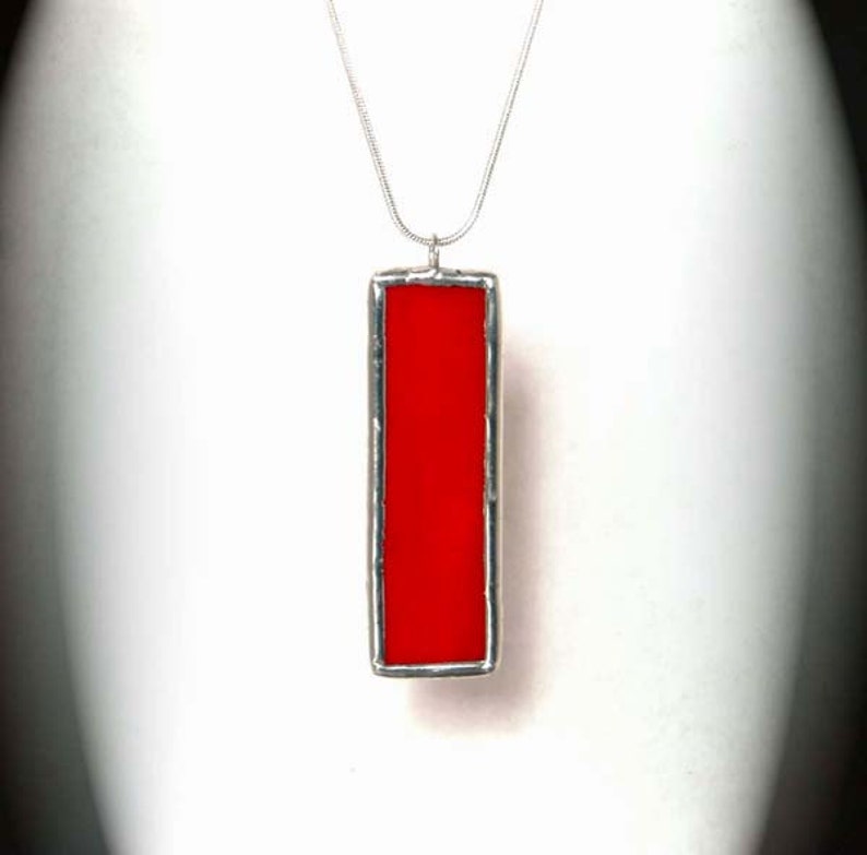 May include: A silver chain necklace with a red rectangular pendant. The pendant is made of stained glass and has a silver frame.