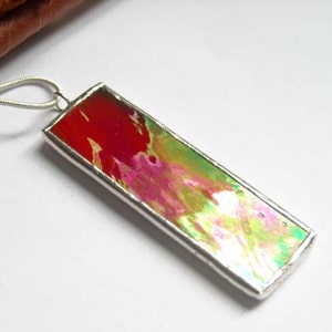 May include: A silver pendant necklace with a rectangular glass charm featuring abstract swirls of red, pink, green, and white.