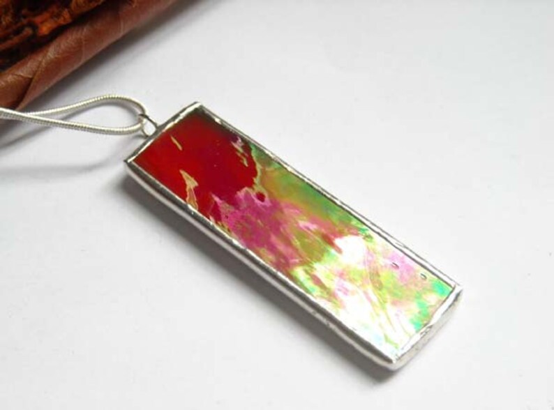 May include: A silver pendant necklace with a rectangular glass charm featuring abstract swirls of red, pink, green, and white.