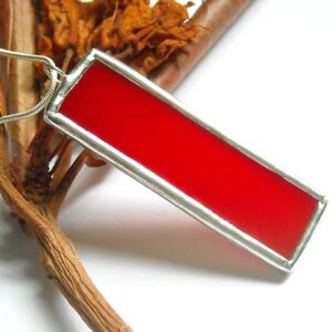 May include: A red glass pendant with a silver frame. The pendant is hanging from a silver chain.