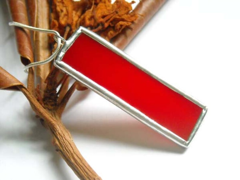 May include: A red glass pendant with a silver frame. The pendant is hanging from a silver chain.