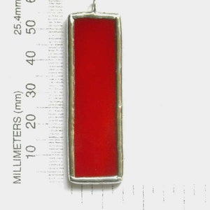 May include: A red stained glass pendant with a silver frame. The pendant is approximately 2 inches tall.