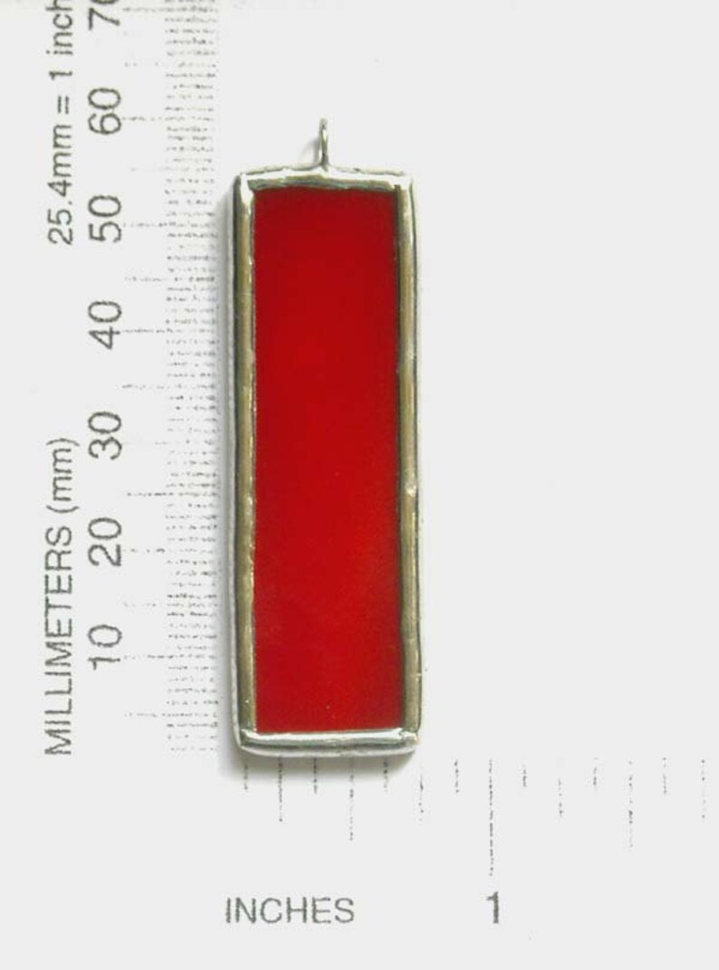 May include: A red stained glass pendant with a silver frame. The pendant is approximately 2 inches tall.