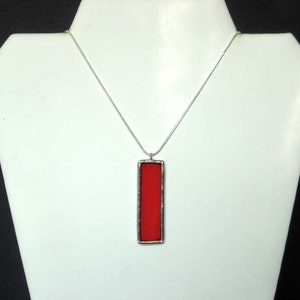 May include: A silver chain necklace with a rectangular pendant featuring a red glass insert.