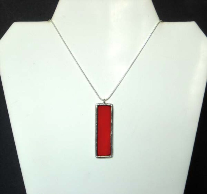 May include: A silver chain necklace with a rectangular pendant featuring a red glass insert.