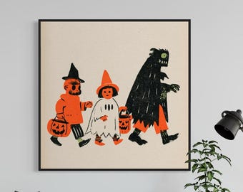 May include: A square framed wall art print featuring a stylized illustration of three figures in Halloween costumes, including a pumpkin-headed character, a ghost, and a dark creature, all carrying orange jack-o'-lantern buckets on a cream background.