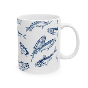 May include: White ceramic mug featuring a repeating pattern of blue fish illustrations. The fish are depicted in a detailed, vintage style, creating a nautical or marine theme. The mug has a standard handle and a glossy finish.