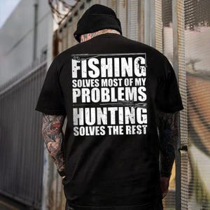 May include: Black t-shirt with white text that reads "FISHING SOLVES MOST OF MY PROBLEMS HUNTING SOLVES THE REST." The shirt has a crew neck and short sleeves. The image shows the back of a person wearing the shirt.