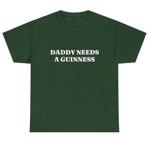 May include: Dark green t-shirt with the white text "DADDY NEEDS A GUINNESS" across the chest. The shirt has a crew neck and short sleeves. The fabric appears to be a soft, comfortable material.