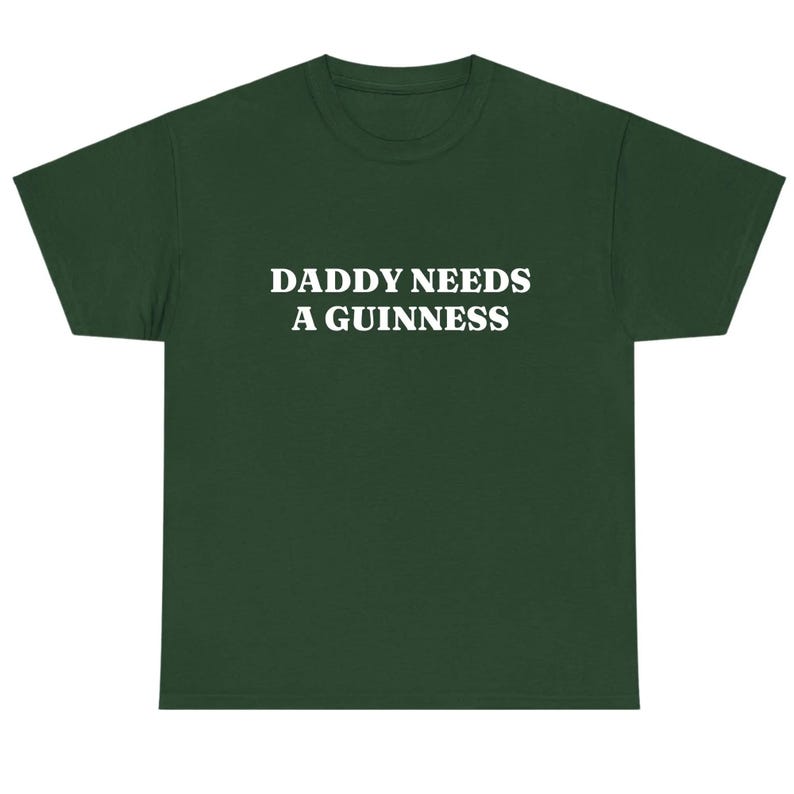 May include: Dark green t-shirt with the white text "DADDY NEEDS A GUINNESS" across the chest. The shirt has a crew neck and short sleeves. The fabric appears to be a soft, comfortable material.