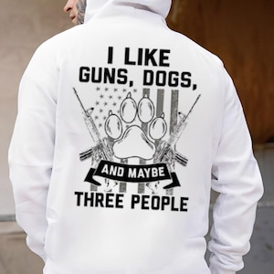 May include: White hooded sweatshirt with the text "I LIKE GUNS, DOGS, AND MAYBE THREE PEOPLE." The design includes a paw print, rifles, and an American flag.