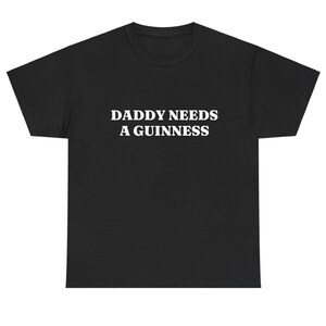 May include: Black t-shirt with the white text "DADDY NEEDS A GUINNESS" across the chest. The shirt is a basic crew neck style, suitable for casual wear. The text is centered and in a bold, sans-serif font.