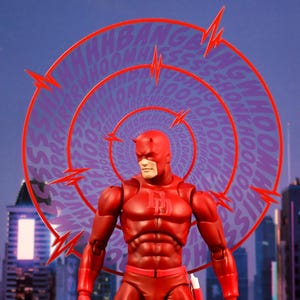 K&ouml;nnte beinhalten: Eine rote und schwarze Daredevil-Actionfigur mit einer roten Maske und einem roten Anzug. Die Figur steht vor einem wirbelnden Hintergrund mit den Worten "Bang", "Whoom", "Ssh" und "Honk", die in einem Kreis wiederholt werden.