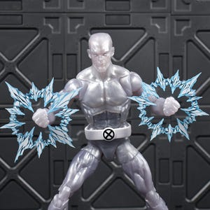 May include: A translucent silver action figure of a superhero with ice-like energy effects emanating from both fists. The figure has a white belt with a black and white circular emblem. The background is a gray, geometric pattern.