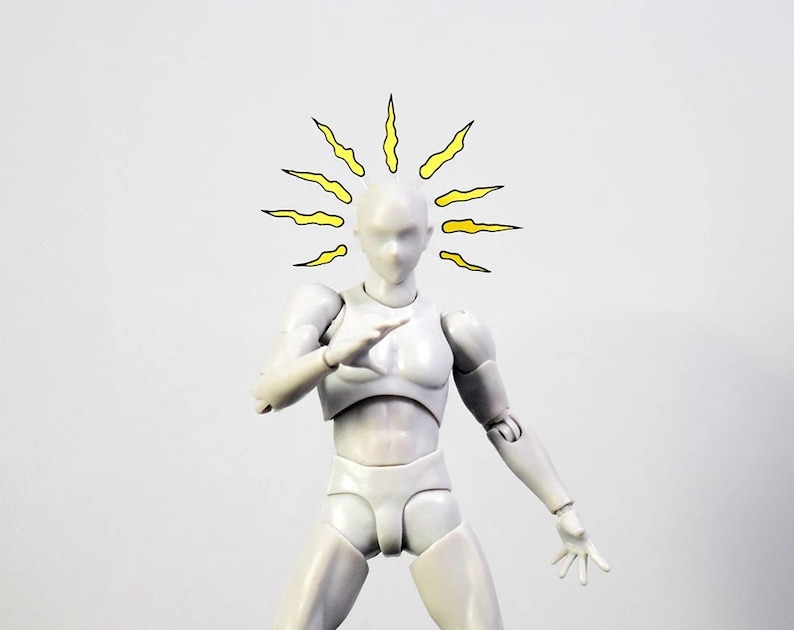 May include: A white plastic articulated figure with a yellow sunburst drawn above its head. The figure is posed with its arms outstretched and its hands open.