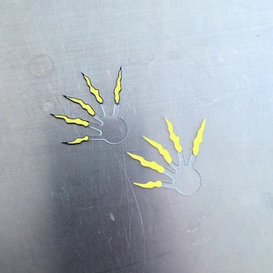 May include: Two yellow claw stencils with black outlines. The stencils are on a gray surface.