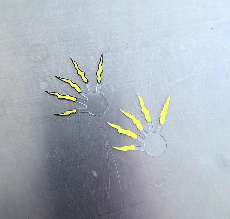 May include: Two yellow claw stencils with black outlines. The stencils are on a gray surface.