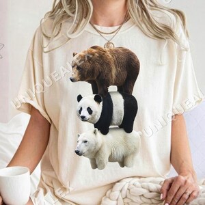 Peut inclure: T-shirt crème avec un motif superposé de trois ours : un ours brun en haut, un panda au milieu et un ours polaire en bas. Le mot "UNIQUEALEX" est imprimé sur le t-shirt.