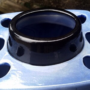 May include: A blue ceramic toothbrush holder with a black rim and multiple holes for toothbrushes.