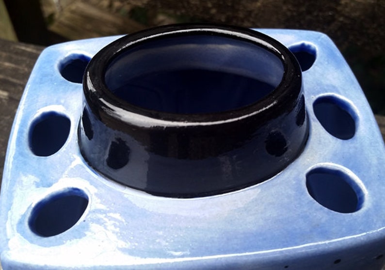 May include: A blue ceramic toothbrush holder with a black rim and multiple holes for toothbrushes.