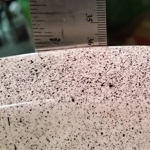 Op de afbeelding: Close-up van een witte keramische kom met een gespikkeld zwart en bruin patroon. De kom heeft een gladde, afgeronde rand.