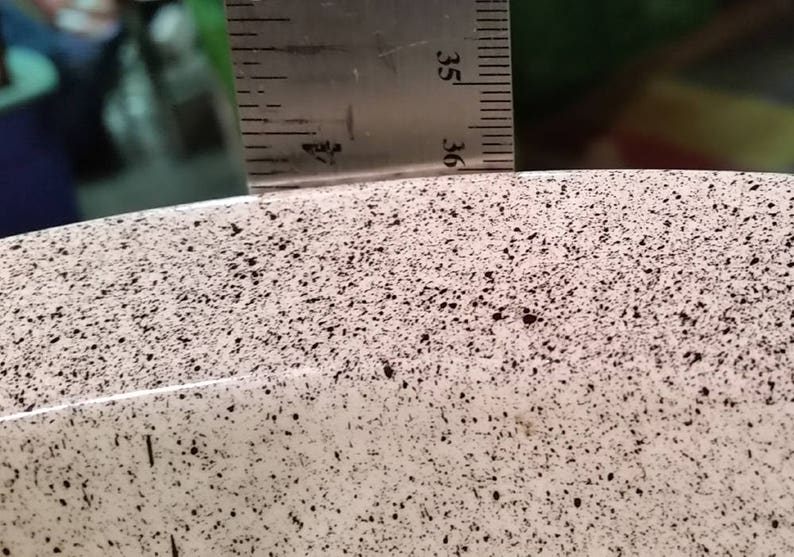 Op de afbeelding: Close-up van een witte keramische kom met een gespikkeld zwart en bruin patroon. De kom heeft een gladde, afgeronde rand.